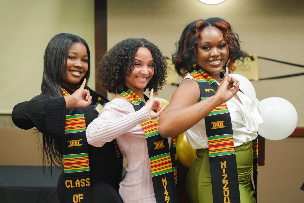 Three graduating scholars pose with the hand signs of the Divine Delta Tau Chapter of Alpha Kappa Alpha Sorority, Inc for a picture together.