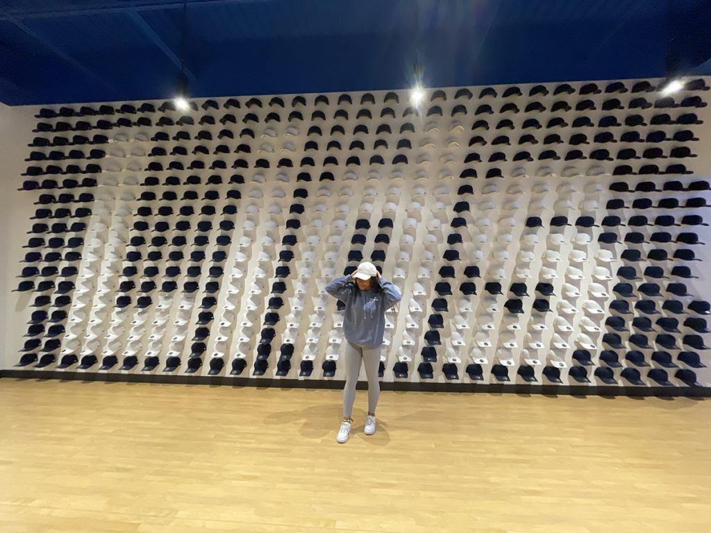 Janae poses in front of the ‘Hat Wall’ at Lids Headquarters on her last day of the internship, August 5, 2022.