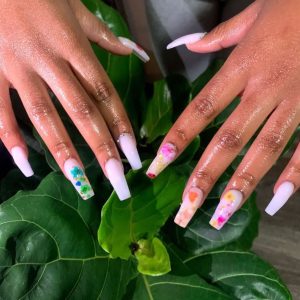 A white nail set with jewels on the cuticle and floral designs done by Bonner when she first started doing nails for her business 'Enhancedbyreese' in 2020. (Photo/Aireeyce Bonner)
