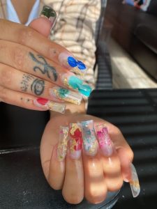 Client N'ya Fritz shows their fresh nails for the camera on Oct. 6. with a set called "The Goddess Look" that has flowers, gold pieces and a squared shape. (Photo/Kailey Williams)