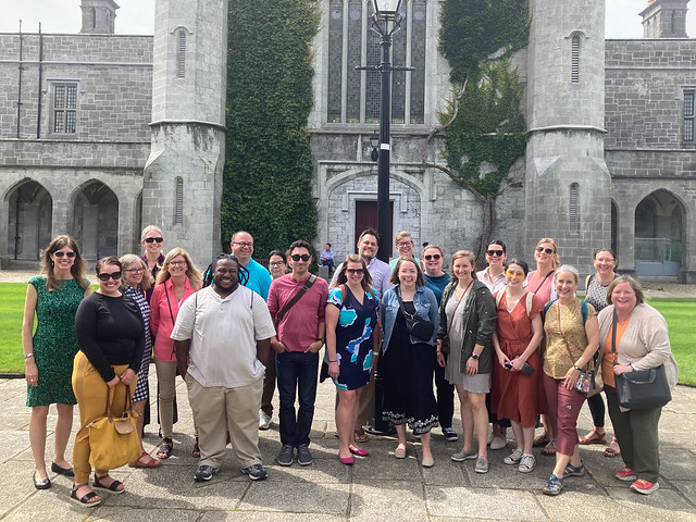 A group of people pose in front of an old, ivy-covered church. 